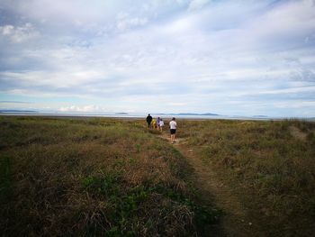 Rear view of family walking on field against sky