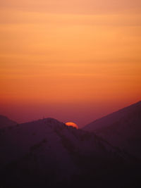 Scenic view of silhouette mountains against orange sky