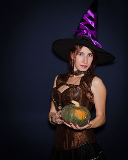 Portrait of woman wearing hat standing against black background