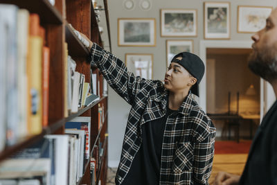 Young man reaching for book by professor in library