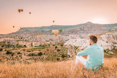 Man looking at view while siting on field against sky during sunset