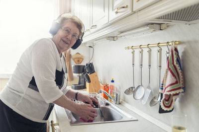 Portrait of senior woman listening music with headphones while washing up