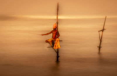 Man holding fishing net against sky during sunset