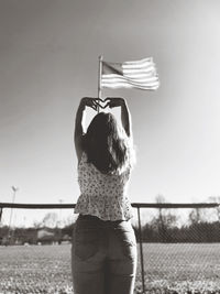 Rear view of girl standing in front of american flag giving heart hands