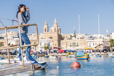 Side view of woman standing against harbor in city