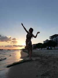 Woman at beach against sky during sunset