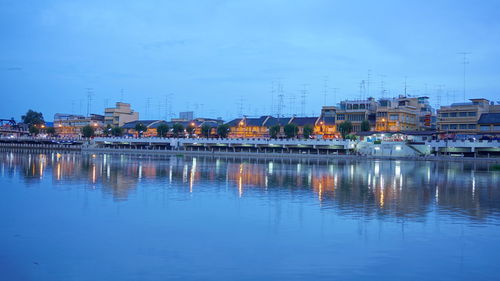 River by illuminated buildings against sky at dusk