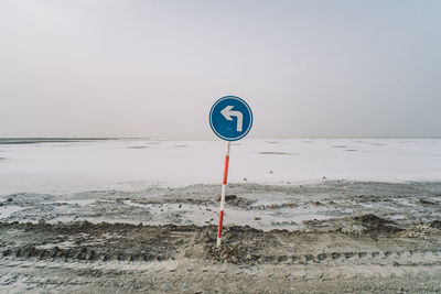 Road sign on beach against clear sky