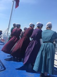 Rear view of women in traditional clothing standing on boat against blue sky
