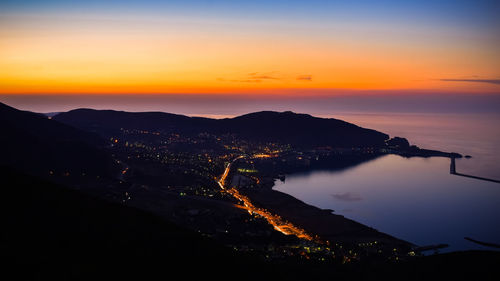 Silhouette cityscape by sea against sky during sunset