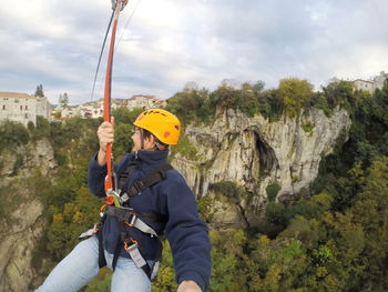 Smiling mature woman hanging on zip line over trees against sky