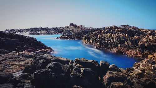 Panoramic view of sea and rocks against clear blue sky