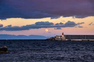 Lighthouse by sea against sky during sunset