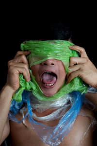Shirtless young man with plastic covering face against black background
