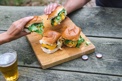 Two unrecognizable hands pick up cheeseburgers from a wooden plate. suburban lifestyle.