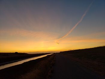 Road amidst field against sky during sunset