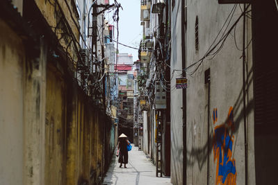 Woman walking amidst buildings at alley in city