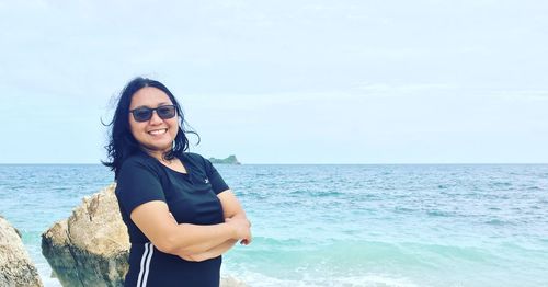 Portrait of smiling young woman standing by sea against sky