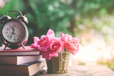 Pink roses bouquet ,clock and book on wooden table over nature green garden in vintage tone 