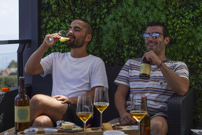 Friends toasting drinks while seating on sofa