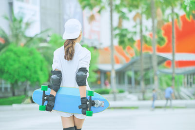 Rear view of woman holding skateboard while standing outdoors