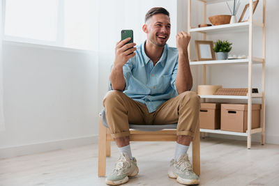 Smiling man holding mobile phone sitting at home
