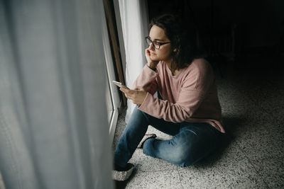 Young woman using mobile phone while sitting on wall