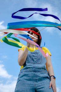 Low section of woman standing against the sky waving with rainbow ribbons. 