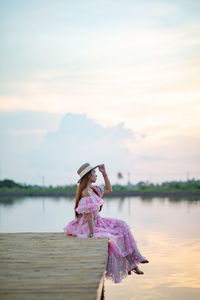 Woman standing on pink lake against sky during sunset