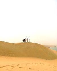 People standing on sand dune in desert against clear sky