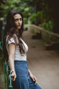 Portrait of smiling woman standing by railing against tree