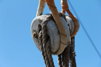 Close-up of ropes on wooden pulley against clear blue sky