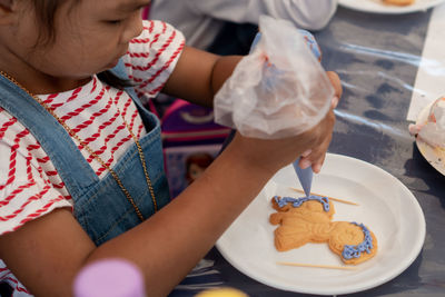 Cute girl decorating cookie with icing in plate on table