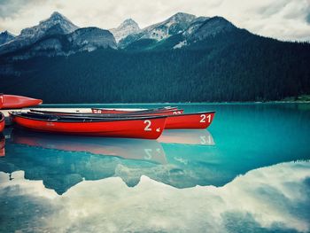 Boat moored on lake by snowcapped mountains against sky