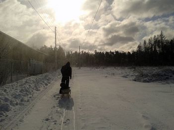 Rear view of father walking child in sledge on snow covered landscape