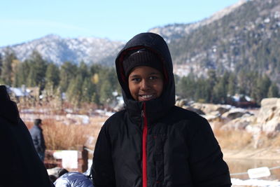 Portrait of smiling boy in warm clothing standing against mountain