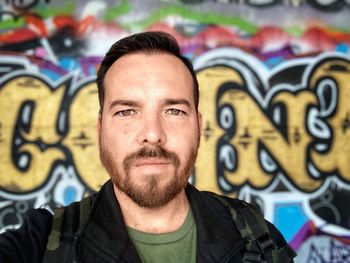 Portrait of man standing against graffiti wall
