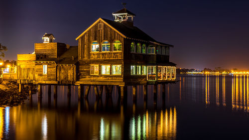 Illuminated house by lake against sky at night