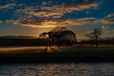 Sun setting behind some trees on the banks of the river eamont with fog forming on the ground