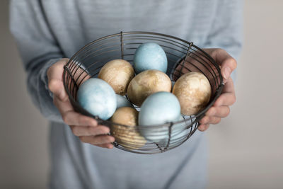 Hands holding colored eggs in wire basket