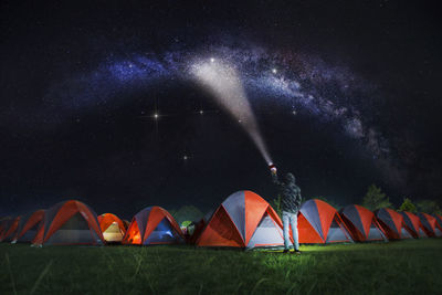 Rear view of man holding flashlight while standing by tents against star field