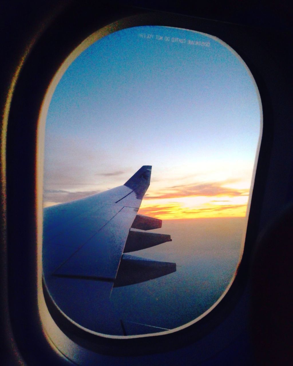 AIRPLANE WING SEEN THROUGH WINDOW DURING SUNSET