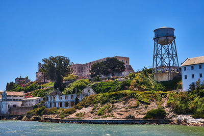 Buildings by river against clear blue sky