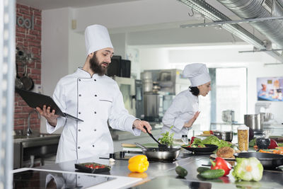 Chef with tablet pc cooking food in kitchen