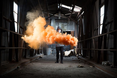 Full length of man holding distress flare while standing in abandoned workshop