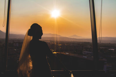 Silhouette woman standing on city against sky during sunset