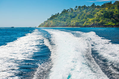 Wave from cruise boat on water surface and horizon with blue sea and island coast at background