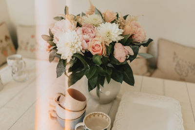 Vase of pastel muted toned flowers on a kitchen table with tea cups