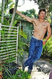 Portrait of shirtless man standing against tree