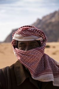 Portrait of man covering face with scarf against sky